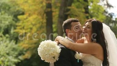 新婚的新娘和新郎高兴地接吻，意识到他们现在结婚了。 以夏季公园为背景的室外拍摄